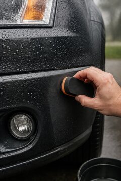 Applying trim restorer to black car bumper with water droplets