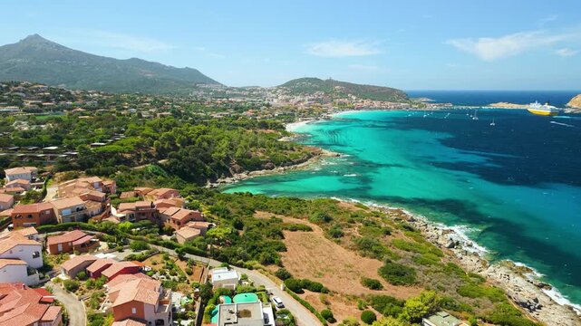 L'Ile-Rousse Corsica island France. Cinematic drone pull back reveal luxury pink villas swimming pools T30 coastal road, turquoise sea rugged coastline resort area, distant beaches view