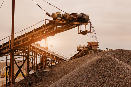 Conveyor belt pouring gravel over large aggregate piles at sand quarry for industrial production and aggregate