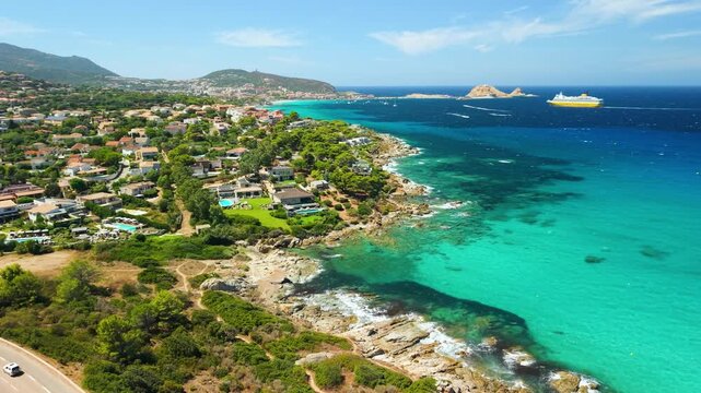 L'Ile-Rousse Corsica drone panning view coastal road ferry harbor turquoise sea, island islet, seaside villas swimming pools rugged coast, left to right sweep Cinematic 4K aerial drone