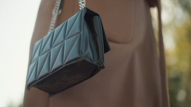 Close up of black quilted leather handbag with silver chain strap hanging from shoulder showing texture detail and stitching. Bag remains primary focus emphasizing its design elements