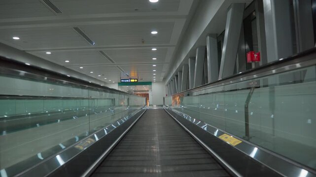 Moving walkway carries the viewer through an empty airport terminal toward a corridor beneath an overhead direction sign