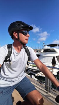 Slow-motion video of an athletic mature man riding an electric bicycle for a healthy and sustainable lifestyle, enjoying the sunny day with a view of boats and the blue sky in the background