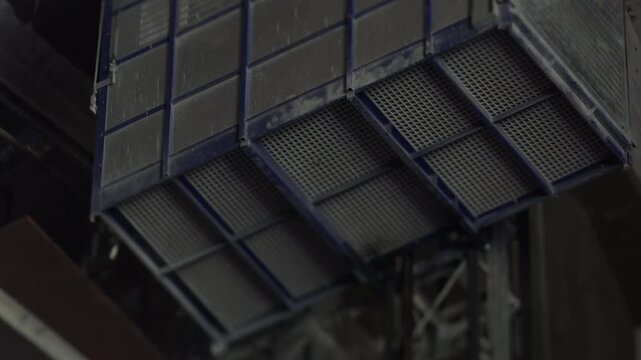 Industrial metal platform hangs beneath a factory ceiling, showing grating panels, steel beams and industrial equipment