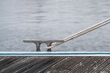 Mooring rope secured to metal dock cleat on marina pontoon with water background © Jane Allan