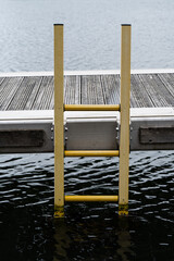 Yellow metal marina ladder descending from wooden pontoon into water © Jane Allan