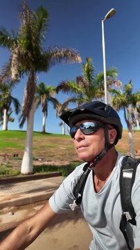 Healthy and active mature man riding his electric bicycle outdoors on a sunny day with palm trees, enjoying freedom and sustainable transportation for positive mental health and well-being