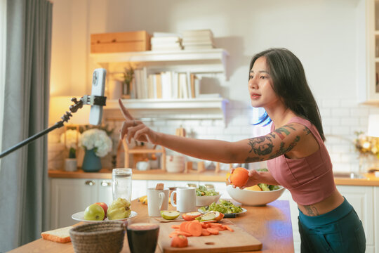 Content creator smiling while live streaming cooking show, food vlogger presenting apple to smartphone camera, healthy eating tutorial recording with neon sign concept