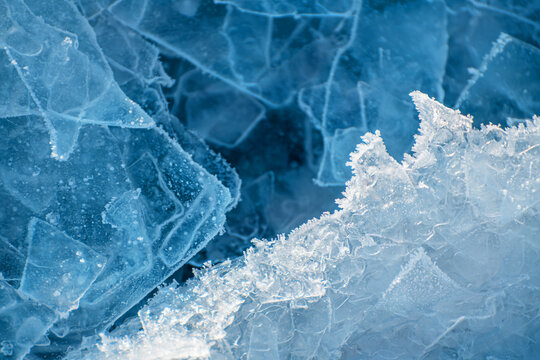 Ice with hoarfrost on the frozen lake at foggy sunrise. Abstract winter nature background.