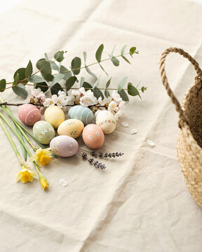 Pastel colored easter eggs arranged with fresh eucalyptus branches and yellow flowers on a white linen tablecloth