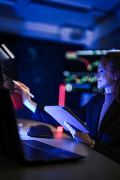 Young businesswoman with long fair hair reviewing program code on a monitor with tablet and stylus marks a bug with the stylus tip at a high tech business conference about artificial