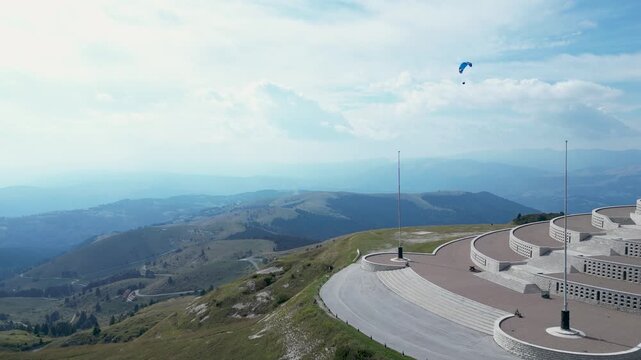 High angle aerial drone view over Monte Grappa war memorial monument under clear blue sky with surrounding mountain peaks in Veneto, Italy