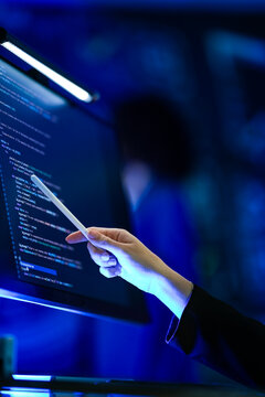 Young businesswoman with long fair hair working with a stylus at monitors of program code marks a bug with the stylus tip in a modern briefing theatre glowing with interactive data graphics