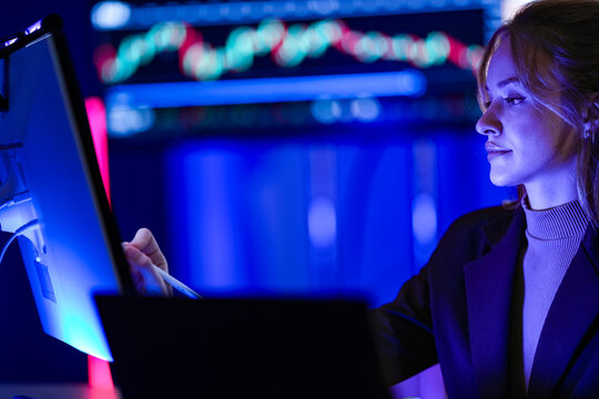 Young businesswoman with long fair hair working with a stylus at monitors of program code scrolls through the source listing in a modern briefing theatre glowing with interactive data