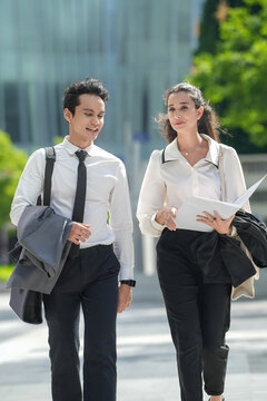 Two business partners in formal suits checking figures in a printed proposal on an open plaza between glass office towers, a documentary style view of professional life in the city