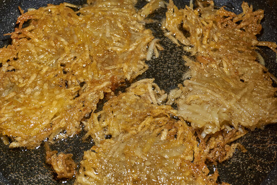 Large grated potato fritter cooking in a frying pan. Hot oil bubbles around the potato pancake as a golden crispy crust forms during frying. Homemade potato pancake made from coarsely grated potatoes.