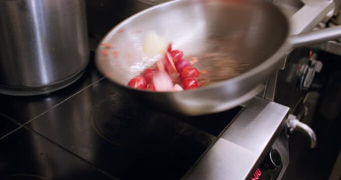 Roasting meal. Tossing pan. Chef hand mixing halved radish with boiling bubbling steaming oil in deep metal wok on electric stove.