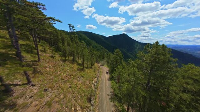 Aerial FPV shot following off road quad bikes on scenic mountain trail