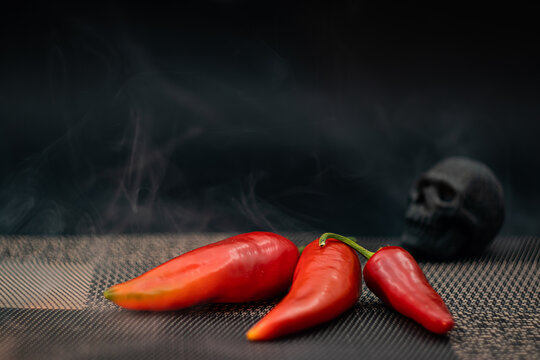 Spicy red chili peppers with smoke and a skull prop on a dark background