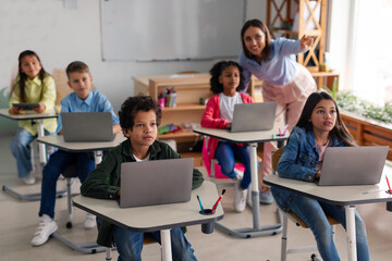 Teacher pointing and explaining lesson to students using laptops, guiding learning process