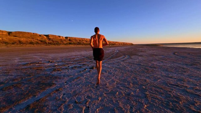 Athletic man jogging on dirt path towards sunset, back view. Great for commercial advertising, documentary, cinematic projects and YouTube.