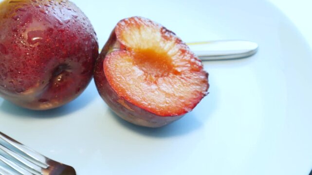 Ripe, juicy plums with fork and knife on a blue plate. Juicy plum cut in a half. Fruits and time of harvesting. Juicy plums sprinkled with water close up.	
