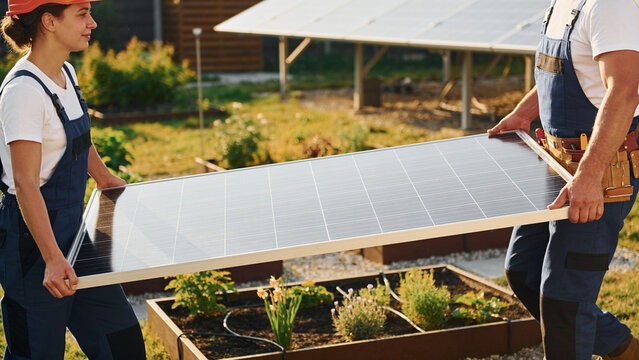 Two installers carrying a solar panel together in a garden