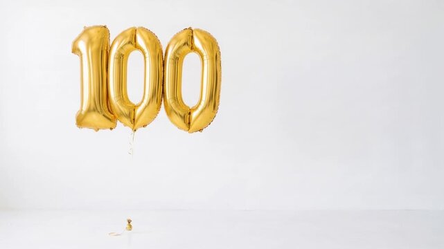 Gold number 100 foil balloons floating on a clean white background with copy space, festive decoration for 100th birthday, centenary, anniversary and milestone celebration.