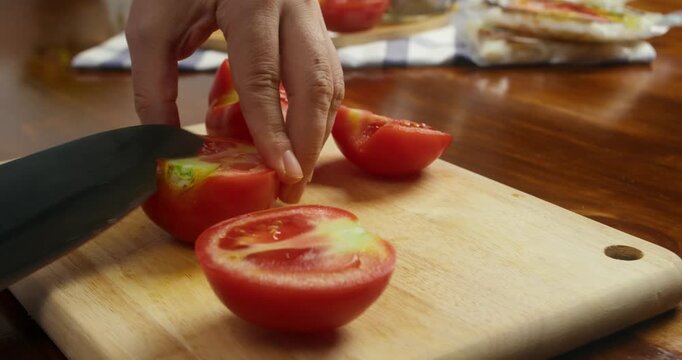 Close up of slicing fresh tomatoes on a wooden cutting board during home cooking. Preparing vegetables and ingredients for a homemade meal in the kitchen.