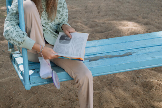 A pretty girl is sitting on a swing and reading a book against a gray background.