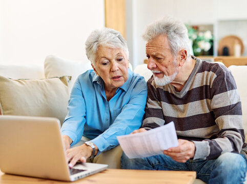 Senior couple checking bills and calculating expenses using a laptop at home, debt taxes concept, worried married elderly couple