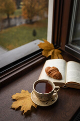 Obraz premium Cozy autumn morning with tea, croissant, and an open book by the window