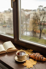 Naklejka premium Cozy autumn morning with tea, croissant, and an open book by the window