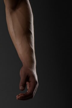 Muscular arm hangs downward against a dark background, showing toned muscles and veins