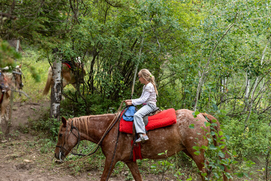 Girl Riding Red Roan Horse on Aspen Forest Trail at Mill Iron Ranch, Wyoming, USA