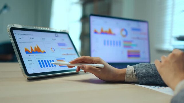 Businessman using digital tablet and analyzing sales performance data and financial charts with a laptop computer in a modern office.