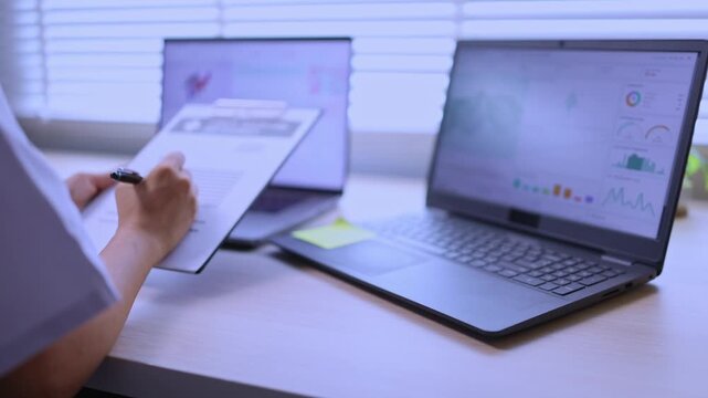 A female doctor in a white coat sitting at her desk, working and analyzing medical data, chemical structures, and graphs on dual laptops in a modern office or clinic setting.