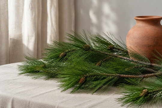 Longleaf pine branches with terracotta urn on linen cloth, natural decor concept