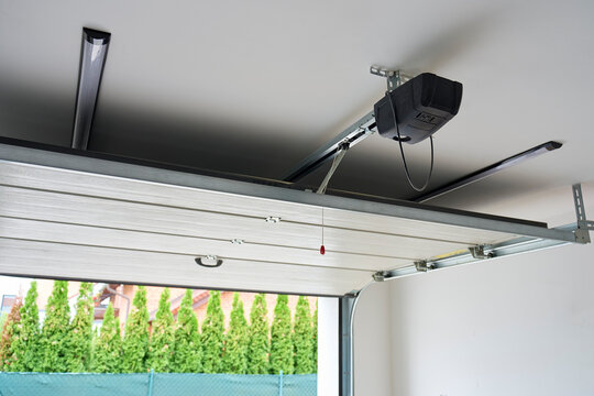 Garage door opener mounted on ceiling above partially open sectional door