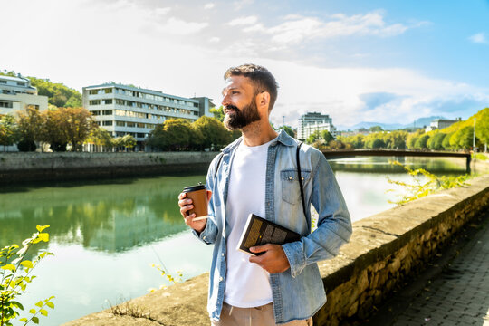 Man enjoying a coffee and book stroll by the river
