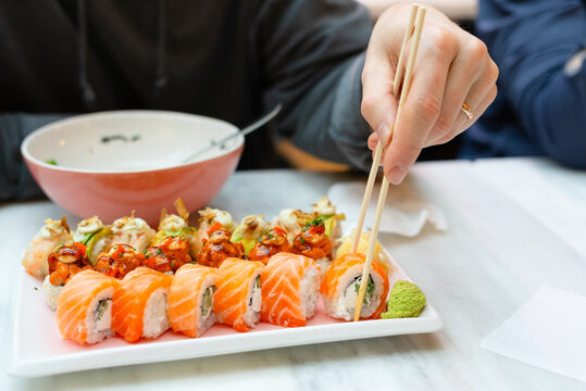 Man picking up sushi with chopsticks at a cozy Japanese restaurant. Diner enjoying authentic taste of fresh rolls during a satisfying meal. Businessman savoring traditional cuisine in inviting eatery