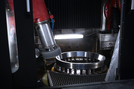 Bearing production. Metal grinding machine with steel ring. Silver spindle head. Dark factory background. Precision manufacturing process