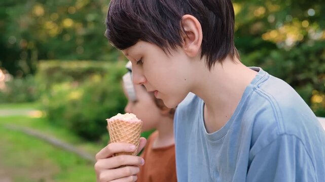 A joyful child savors a sweet treat while holding an ice cream cone in a sunny park. This little boy finds pure bliss eating outdoors, capturing simple summer happiness.