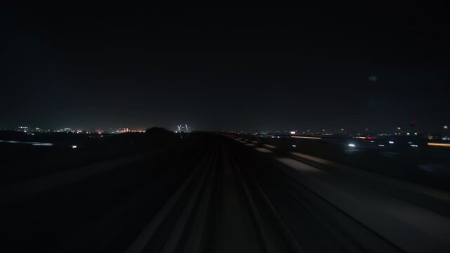 Front train POV travels forward along an elevated metro railway track toward distant city lights into the dark night