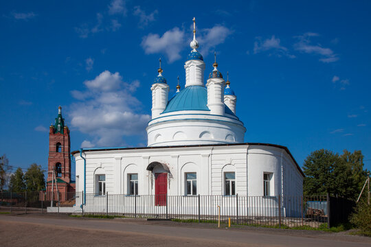 White Orthodox church with blue domes decorated with golden stars and topped with crosses, photographed beneath a deep blue sky with scattered clouds.
