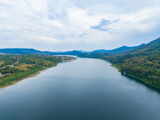 Fototapeta premium River flows through green hills under cloudy sky in an open landscape nearby the mountains