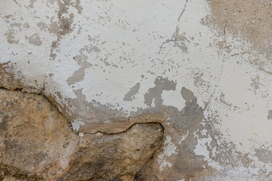 Close-up of white textured wall with peeling paint and exposed stone