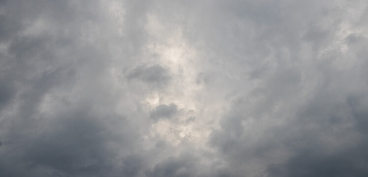Gloomy stormy sky with heavy gray clouds and faint light breaking through