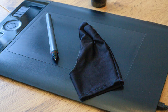 Digital pen and a black drawing glove rest on a black graphics tablet. Digital illustration and design process