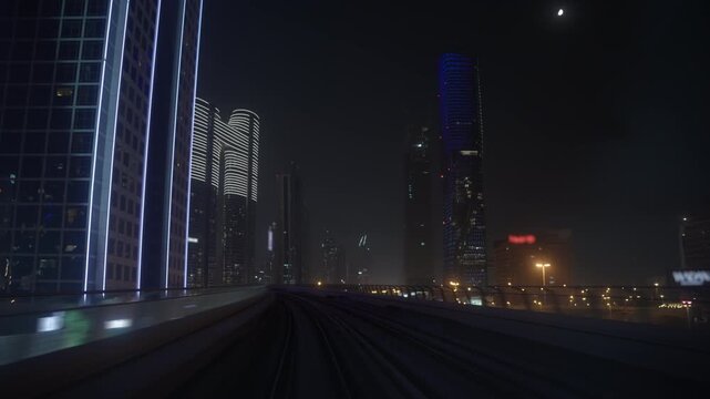 Metro train POV travels along an elevated railway through Dubai, passing illuminated skyscrapers and traffic on Sheikh Zayed Road at night